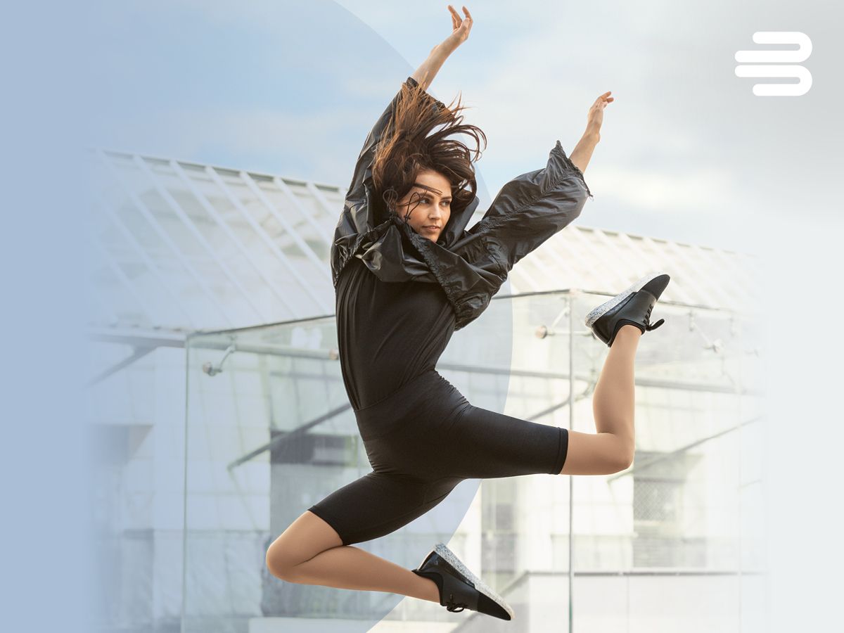 Sportlich gekleidete Frau in dynamischer Sprungpose vor modernem Glasgebäude