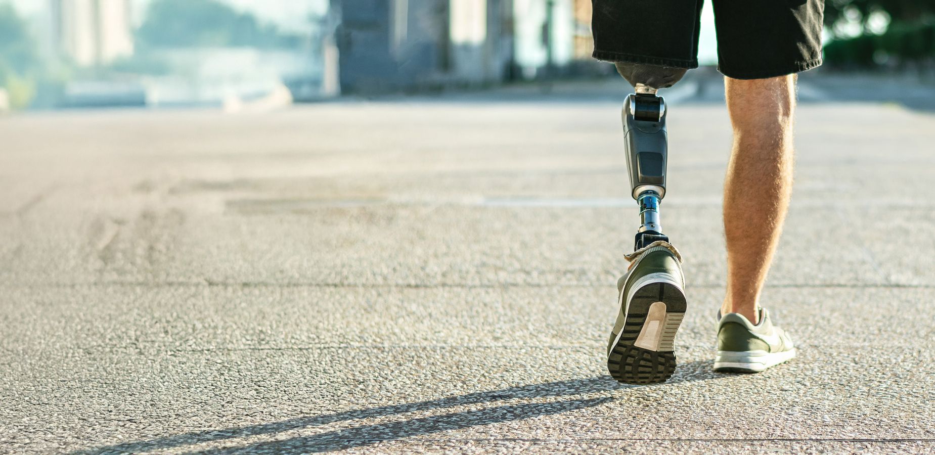 Mann mit Beinprothese geht in Sportschuhen auf einer asphaltierten Straße.